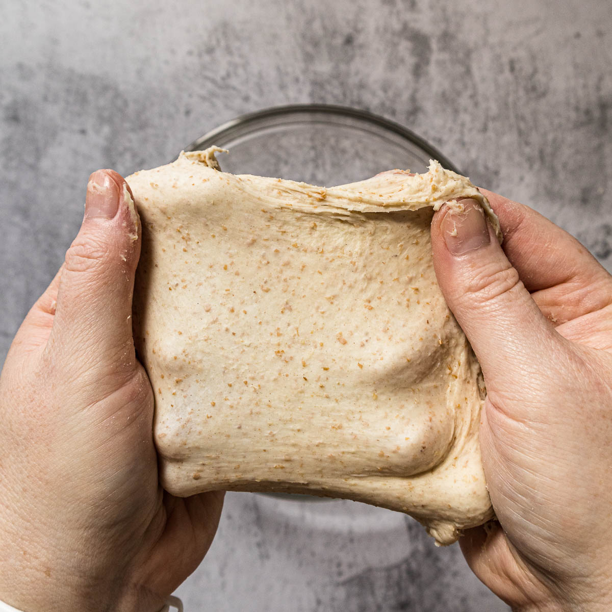 Hands pulling apart a small piece of dough to show the window pane test.