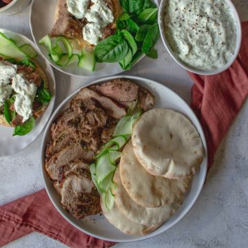Roast leg of lamb carved and plated next to pitas.