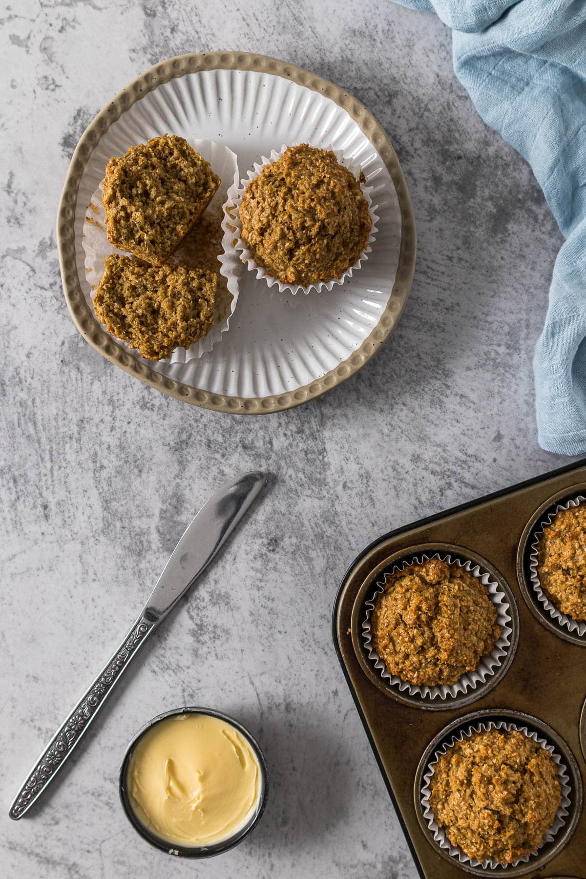 Bran muffin broken in half on a plate with a pat of butter in a small bowl.