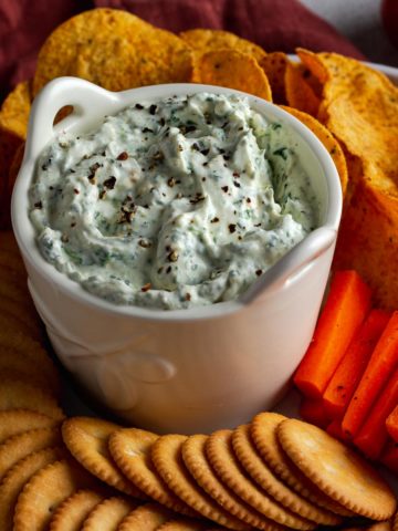 Spinach and Feta Dip surrounded by crackers, chips and carrots.