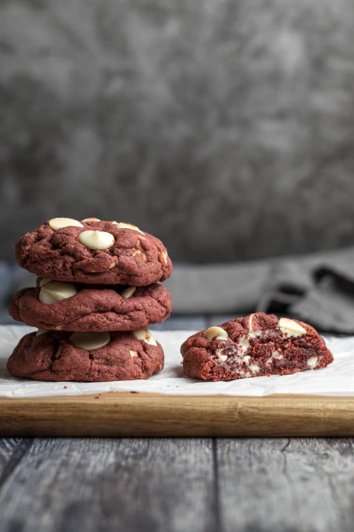 Stacked red velvet cookies next to a cookie sliced in half.
