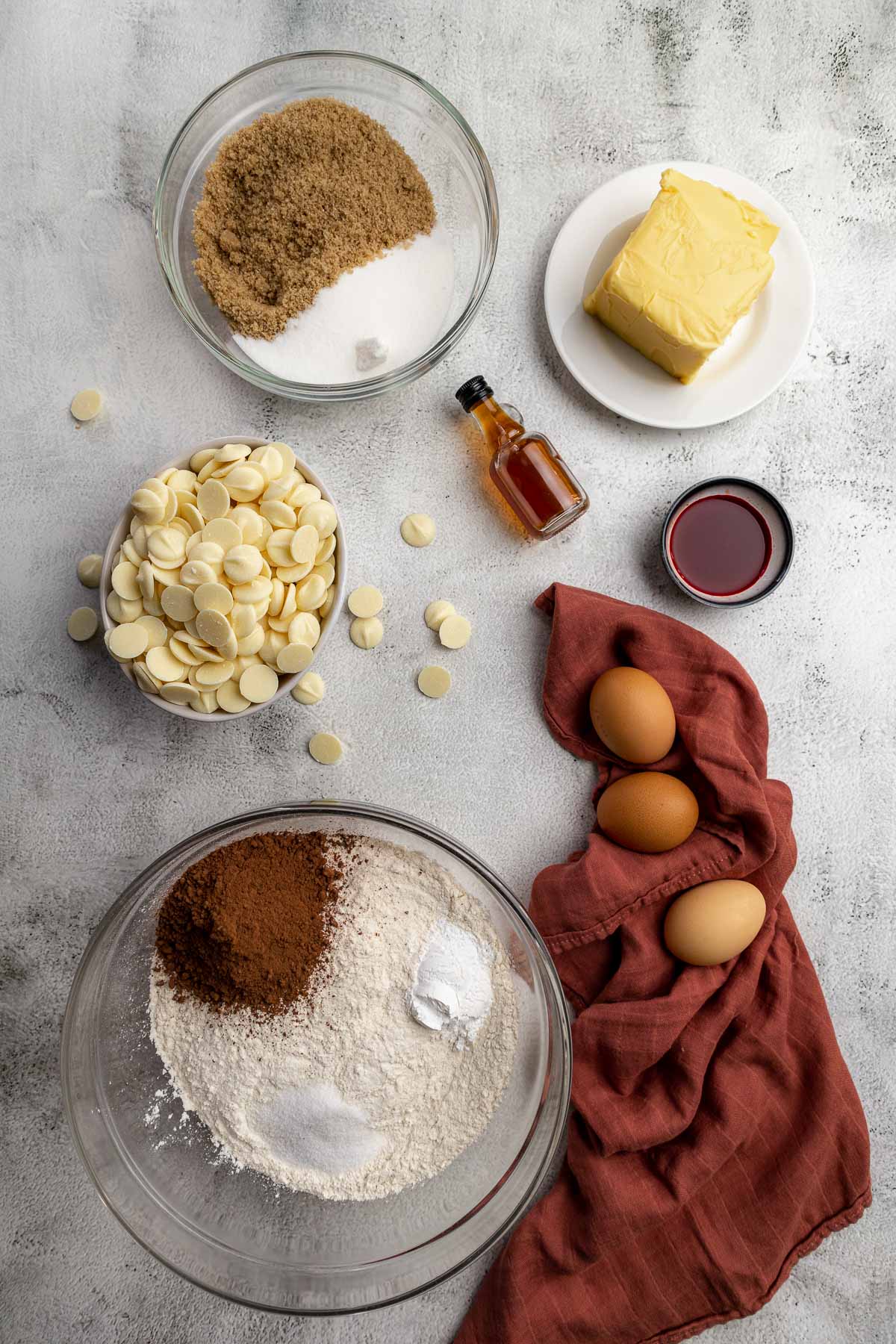 Red velvet cookie ingredients - brown sugar, white sugar, butter, white chocolate chips, vanilla, red food colouring, flour, baking powder, salt, cocoa powder