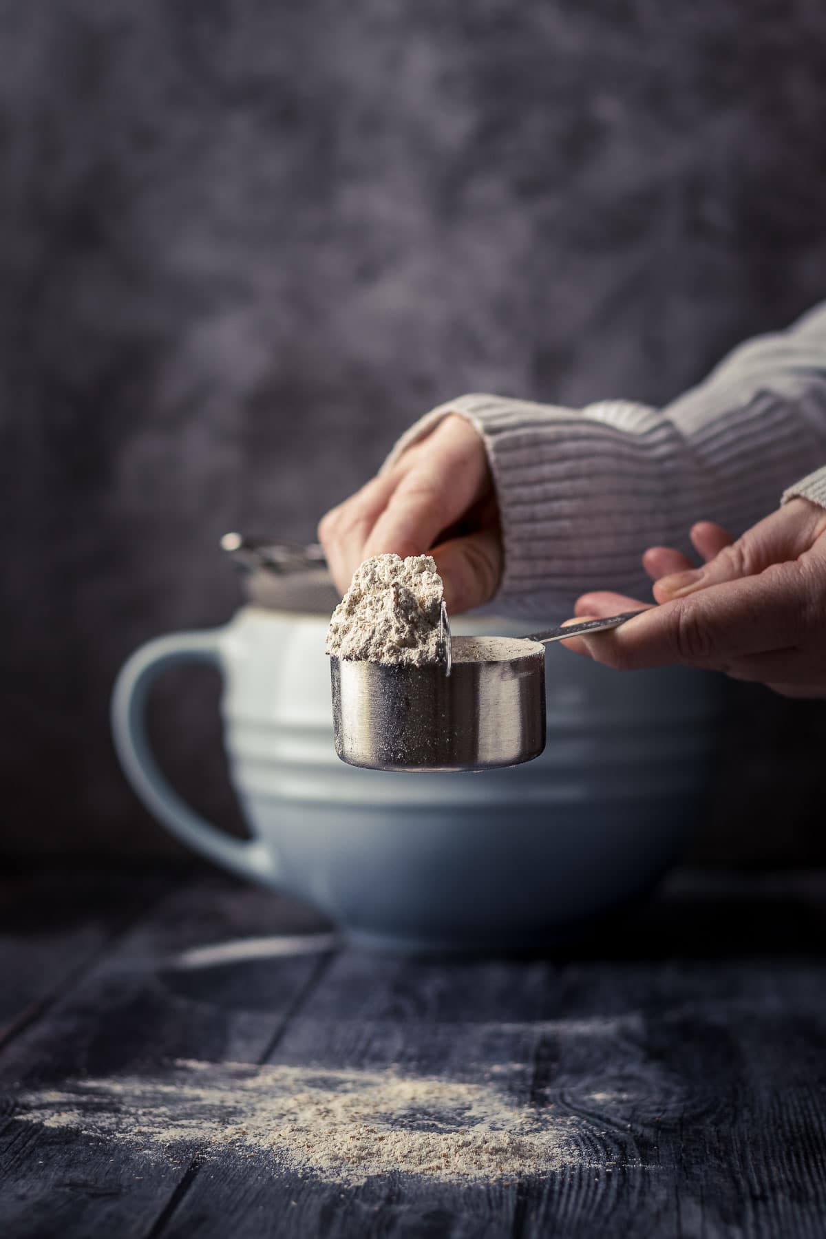 A hand pushing off the excess flour from a measuring cup with the back of a knife.