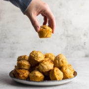 Hand picking up a mini cheese muffin from a plate.
