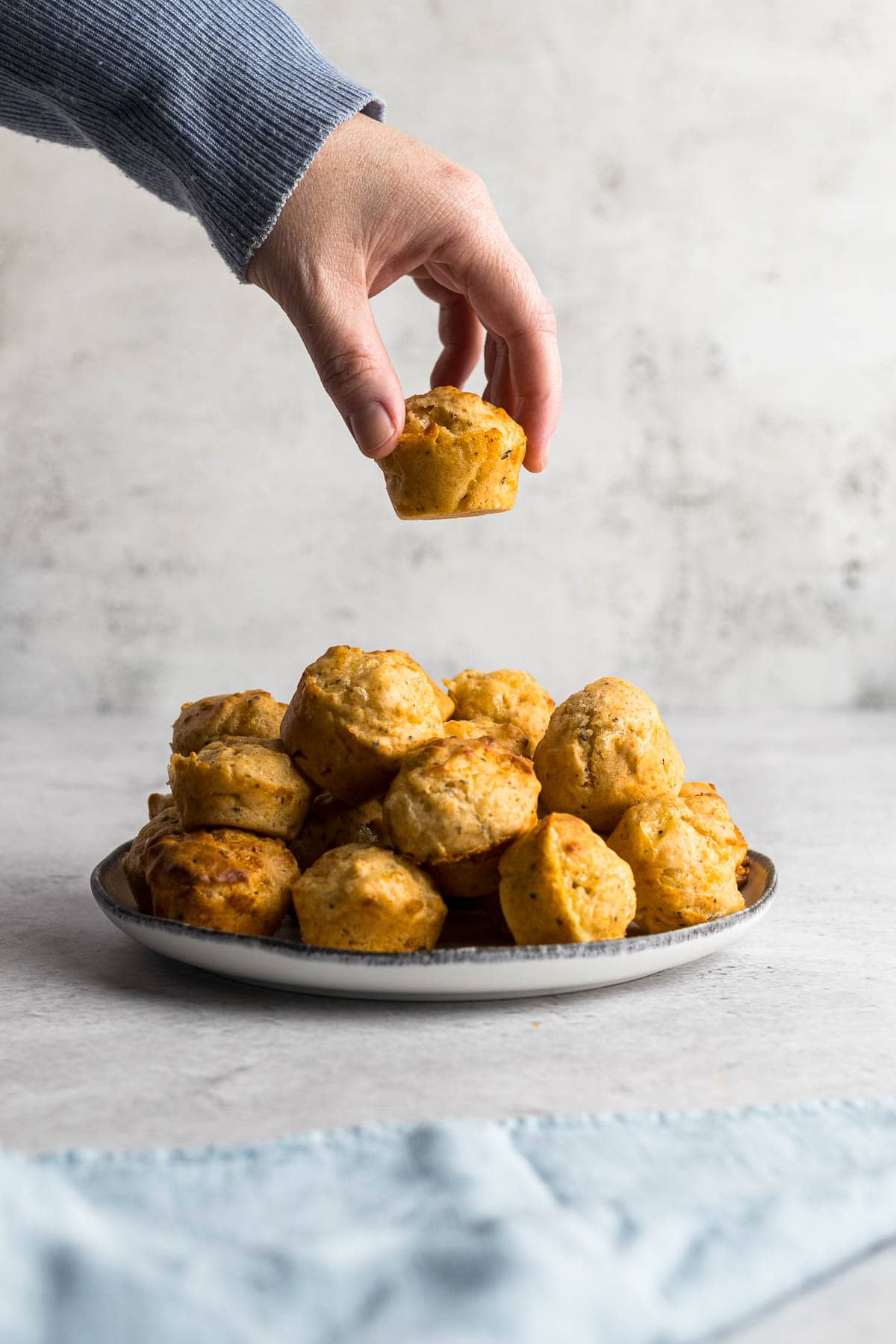 Hand picking up a mini cheese muffin from a plate.