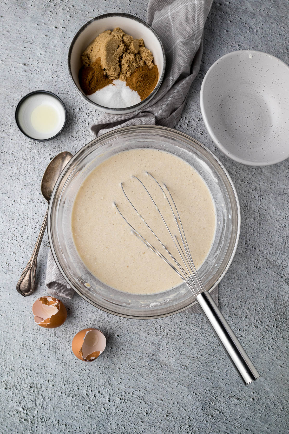 Pancake batter in a mixing bowl next to cinnamon sugar, eggshells.