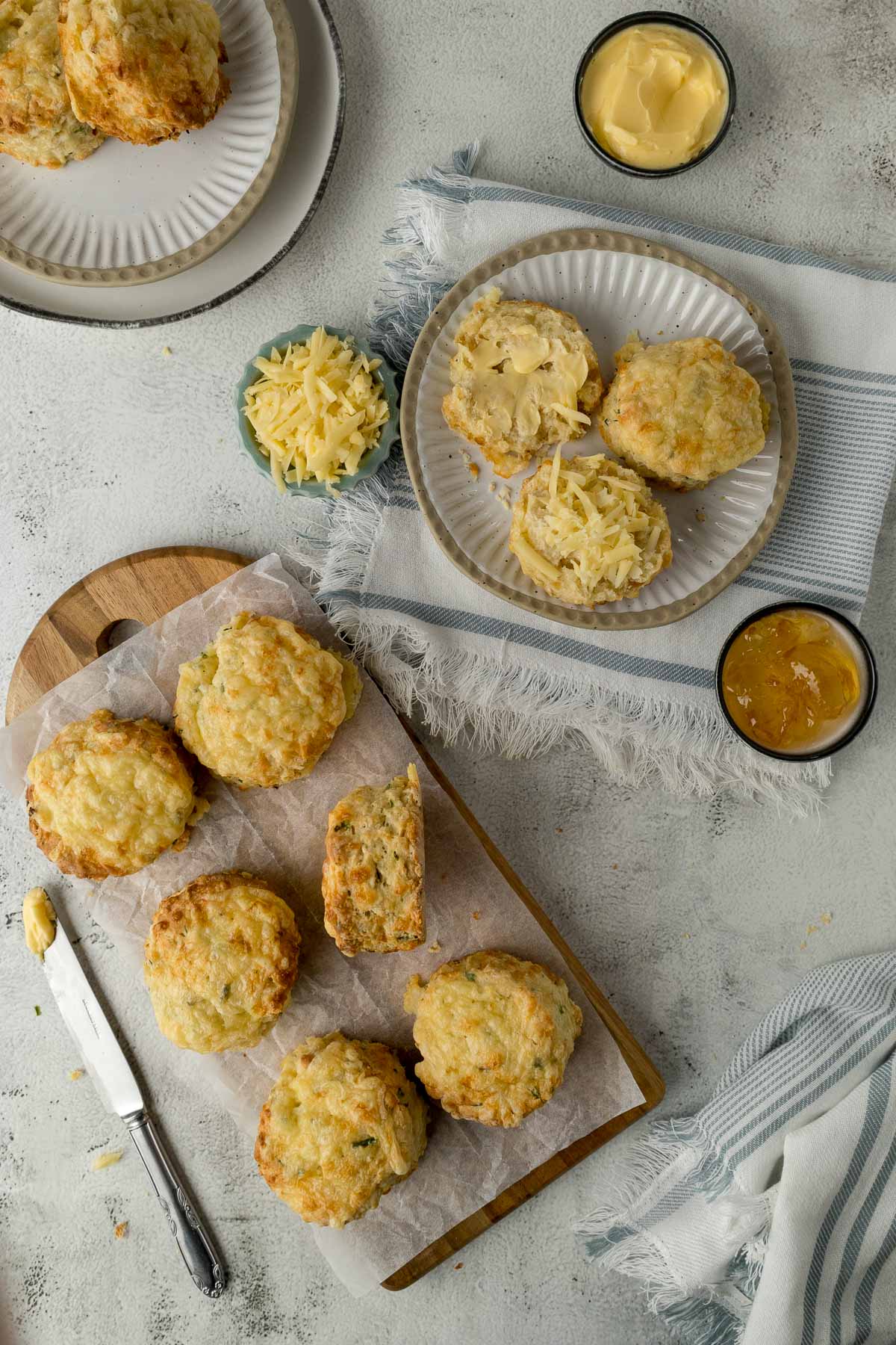 Scone cut open with butter and cheese next to scones on a platter.