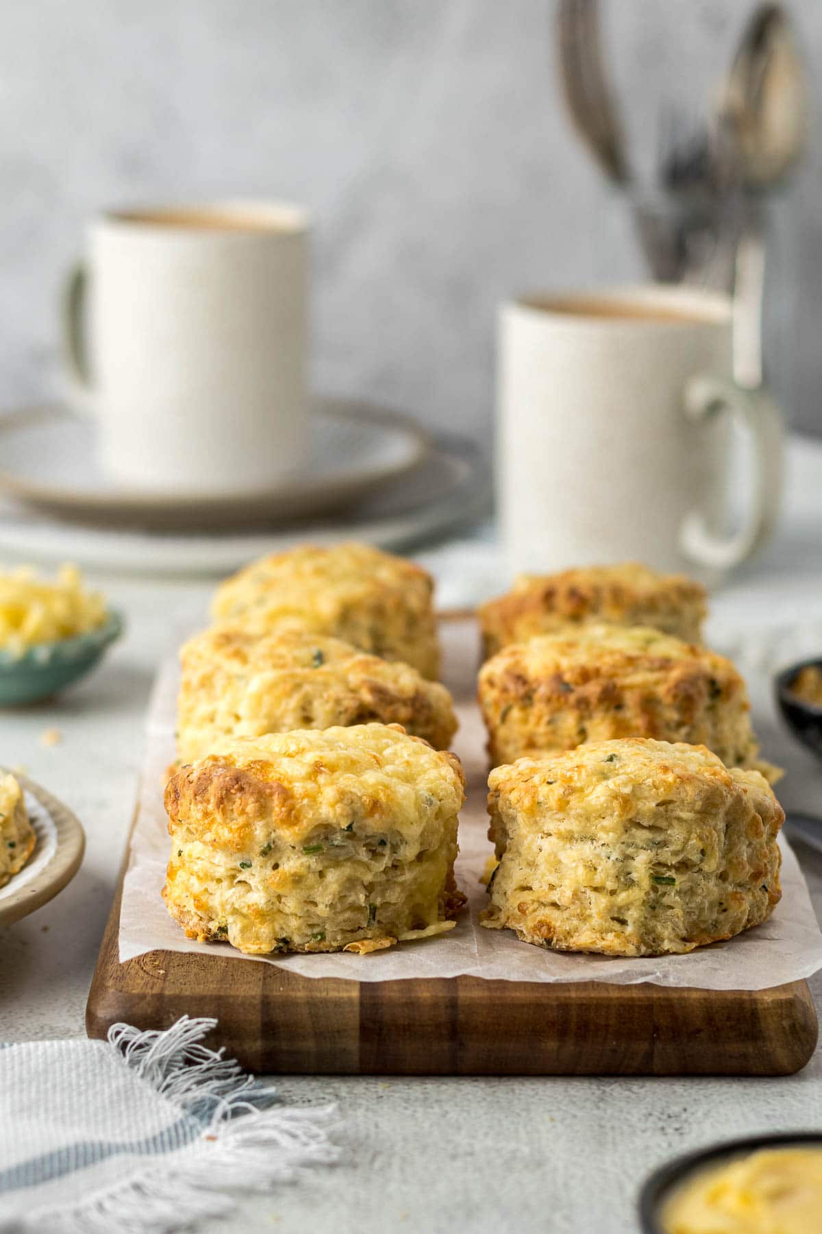 Cheese and chives scones on a platter with cups of tea in background.