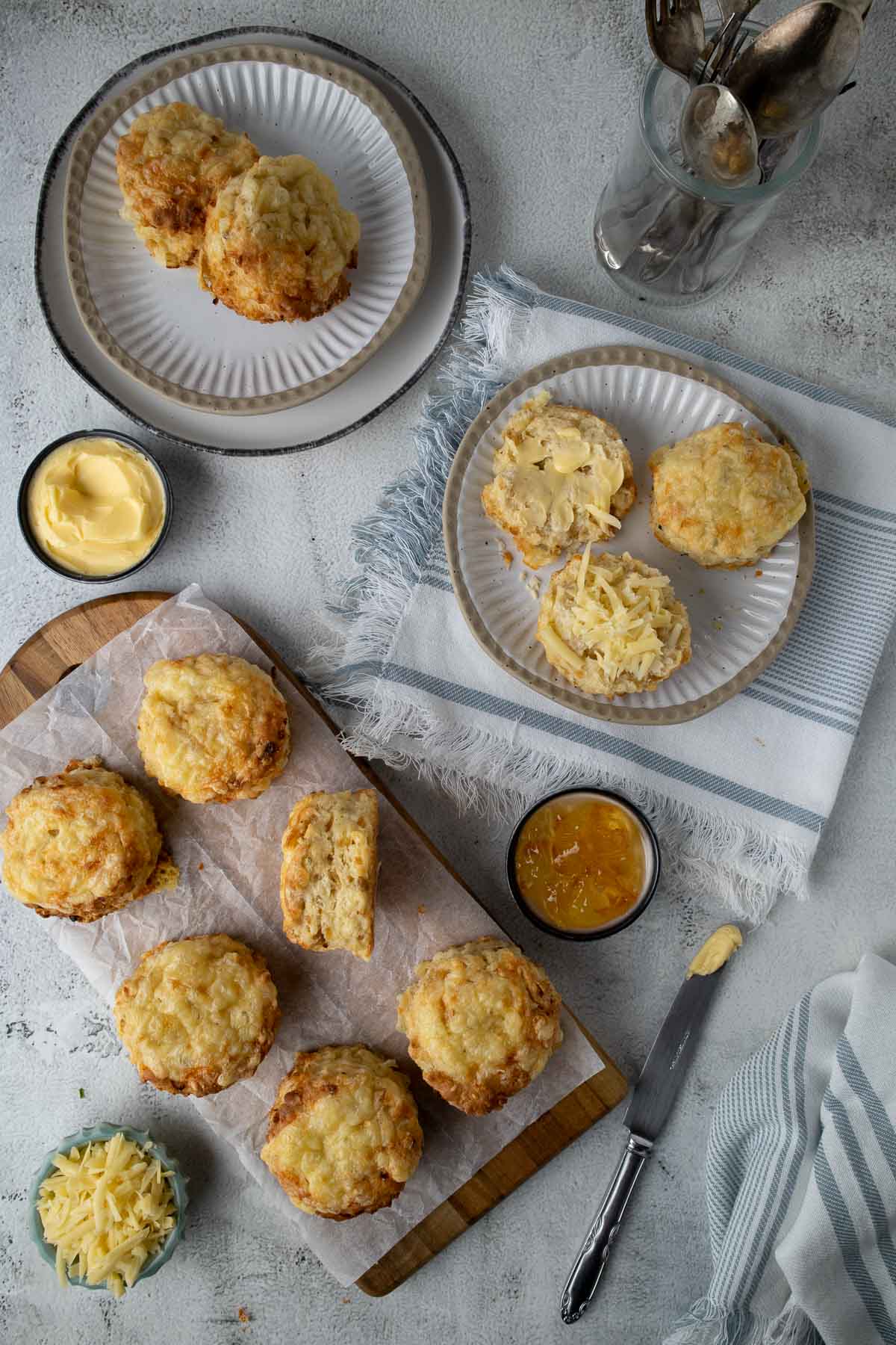 Cheese and onions scones on a table, with one cut open served with butter, cheese and marmalade.