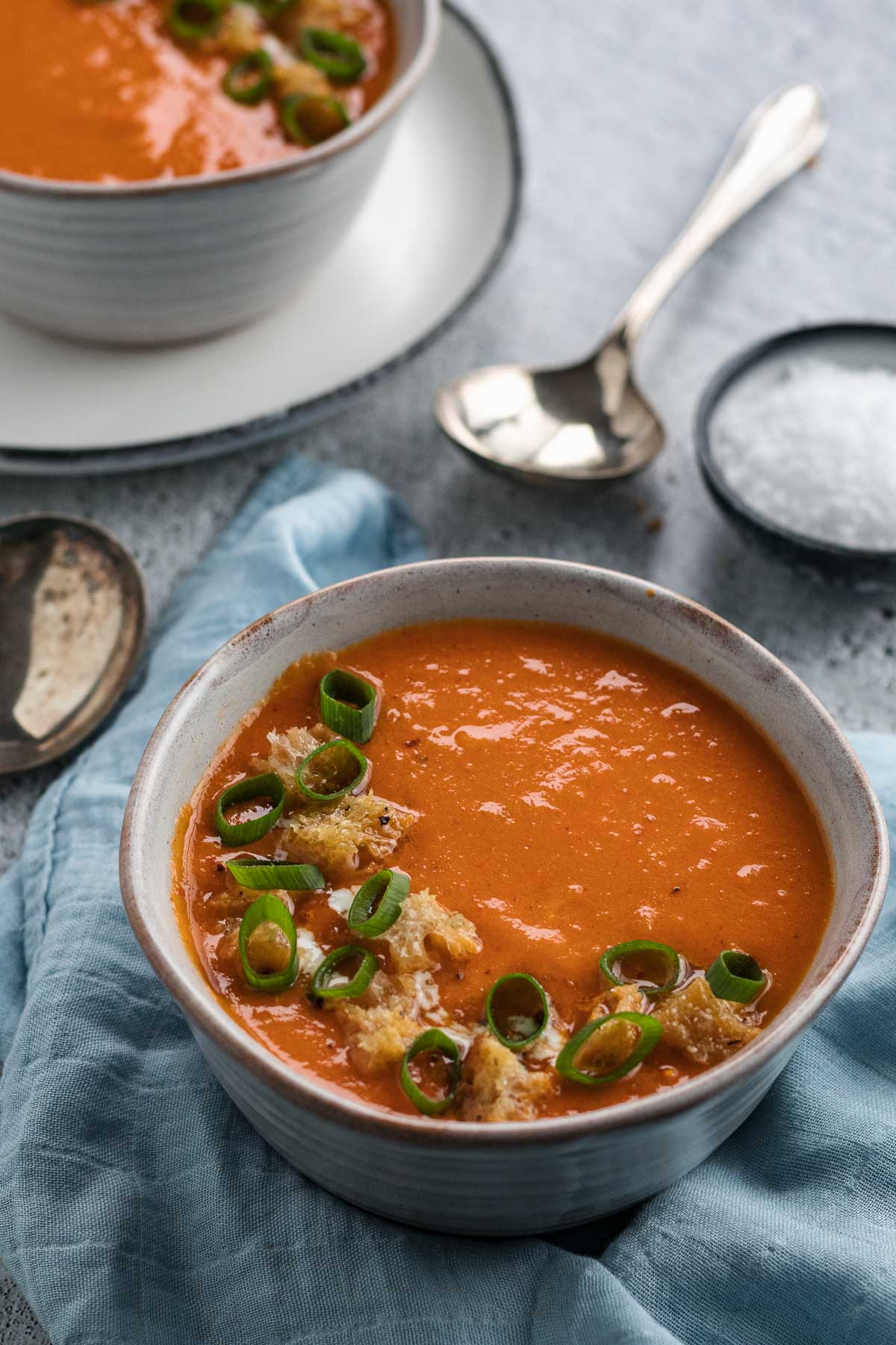 Bowl of roast tomato soup with croutons on a blue napkin.