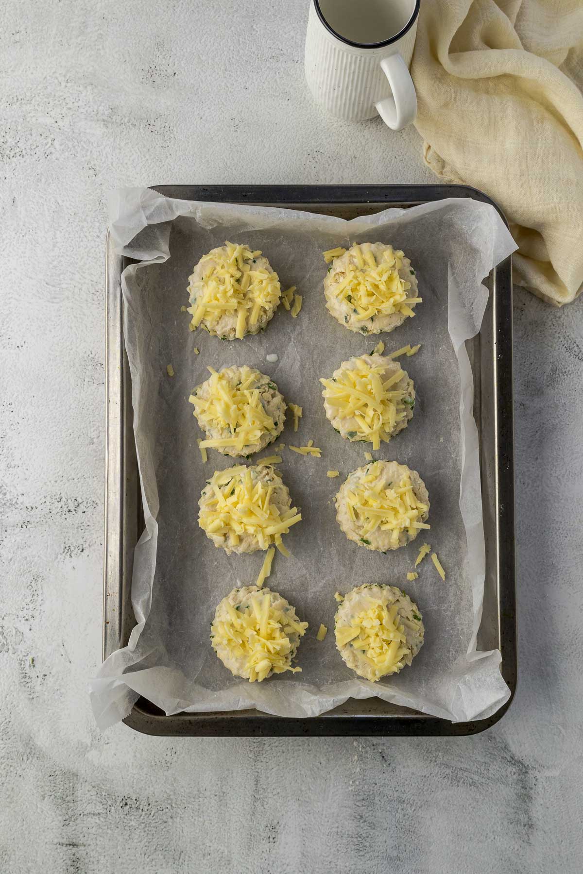 Scones brushed with milk and topped with cheese on a baking sheet.