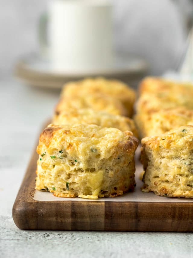 Close up of cheese and chives scones on a board with a cup in the background.
