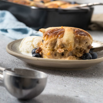Portion of hot cross bun pudding on a plate with ice cream.