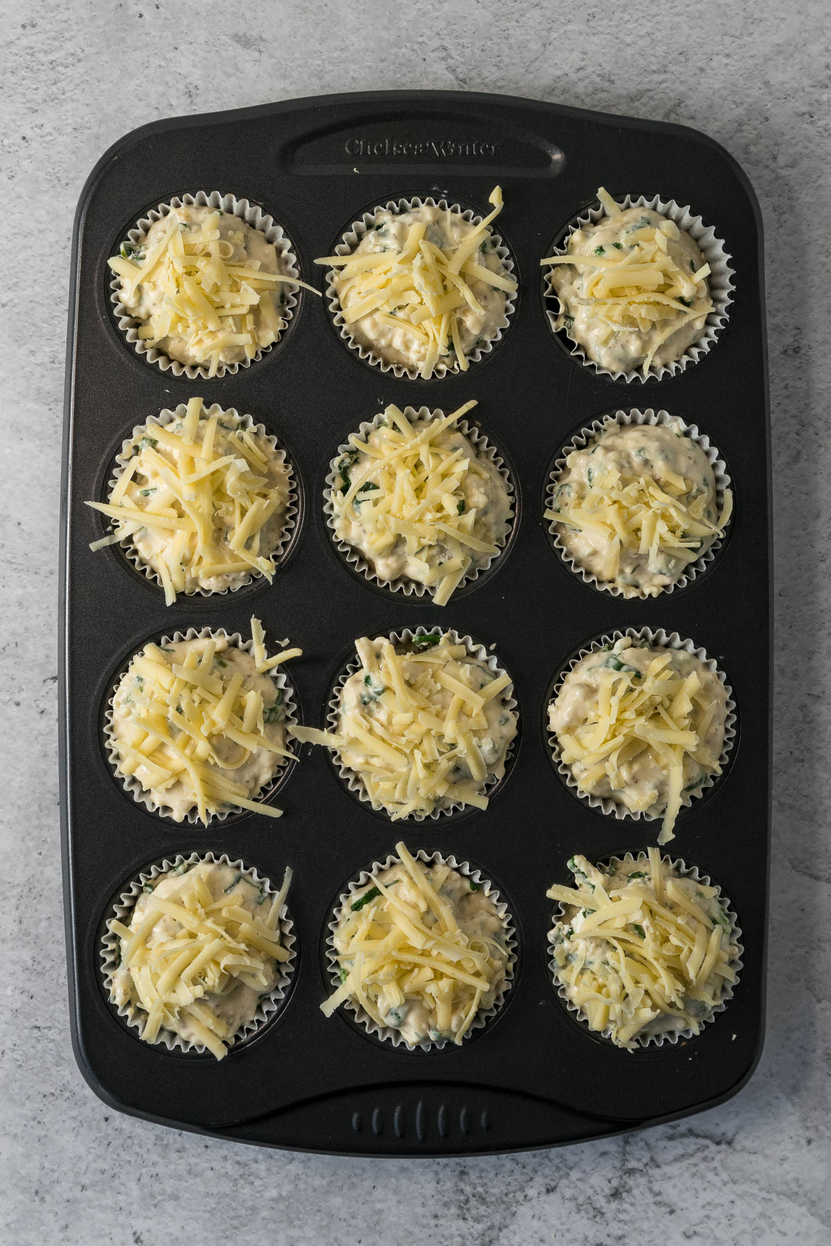 Muffin batter divided into liners and topped with cheese.
