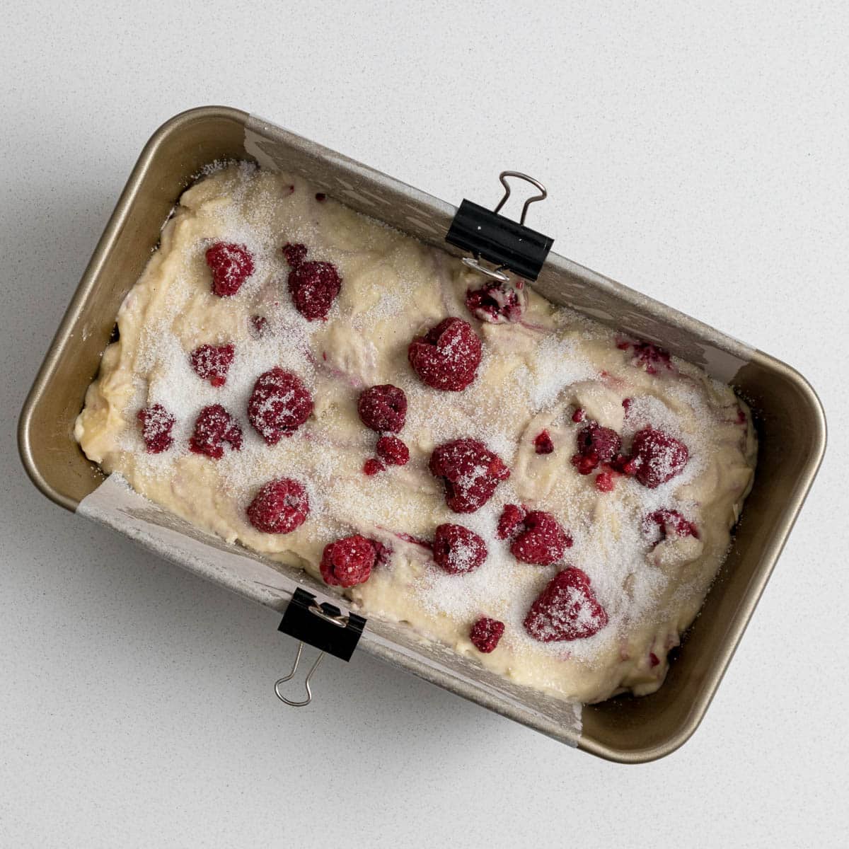 Cake batter topped with raspberries and sugar.
