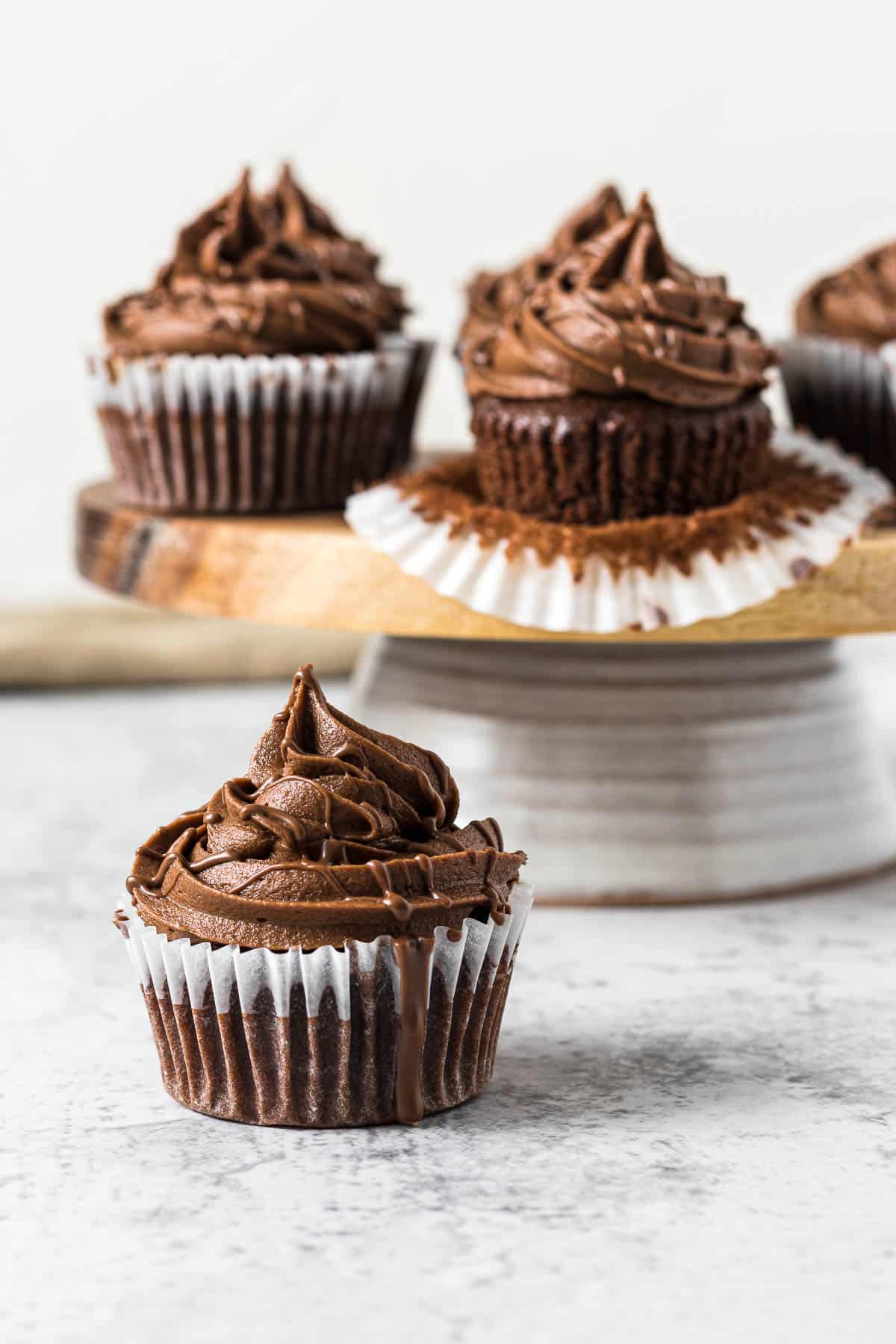 Frosted nutella cupcake with a nutella drizzle in front of a cake stand.