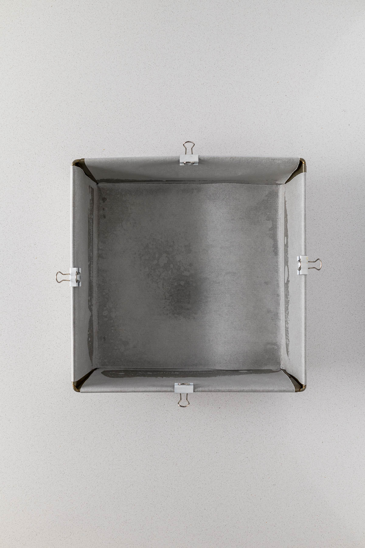 A 9"x9" square cake tin lined with baking paper overhanging the sides.