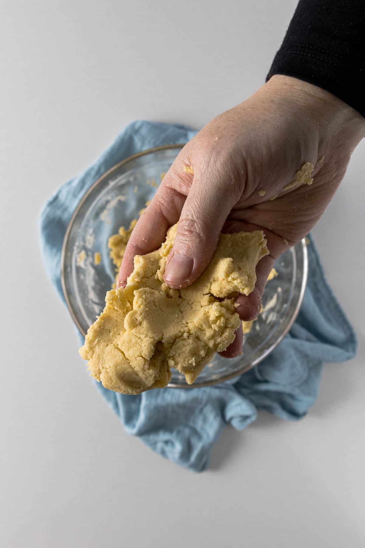 Soft pliable shortbread biscuit dough being held up to the camera.
