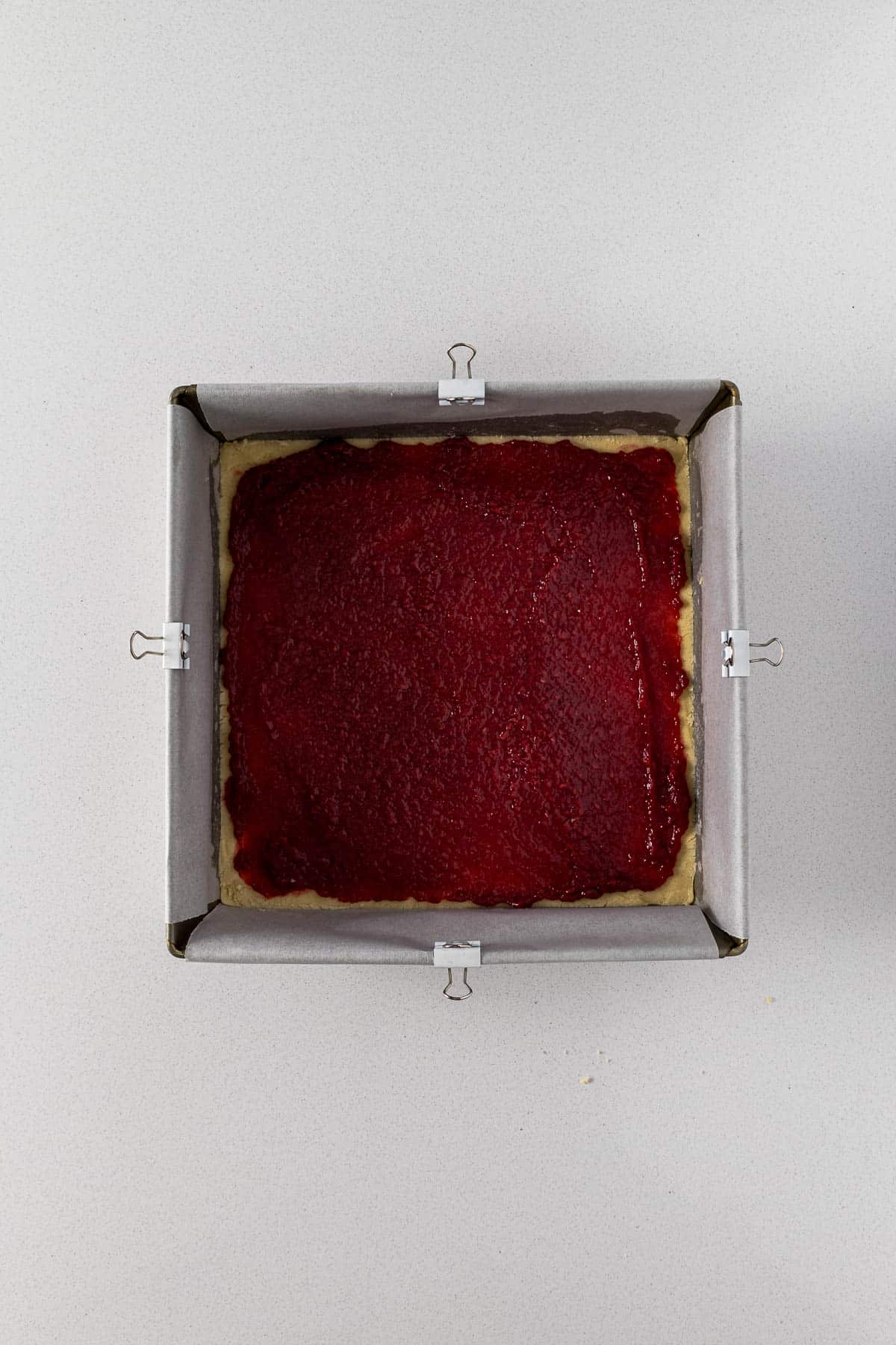Jam spread over the biscuit dough pressed into the tin.