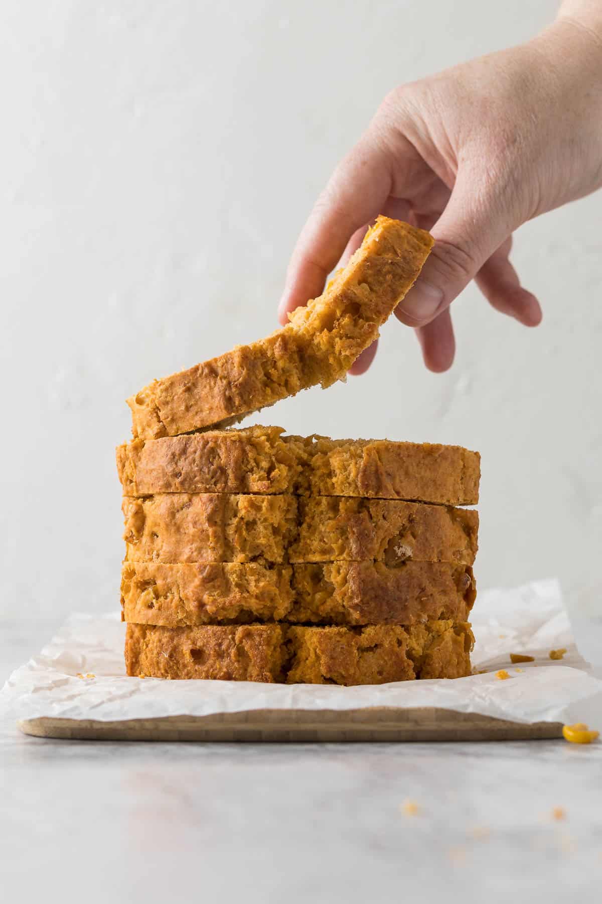 Hand picking up a slice of mealie bread from the bread board.