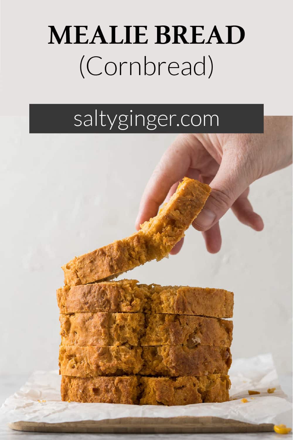 Hand picking up a slice of mealie bread from a cutting board.