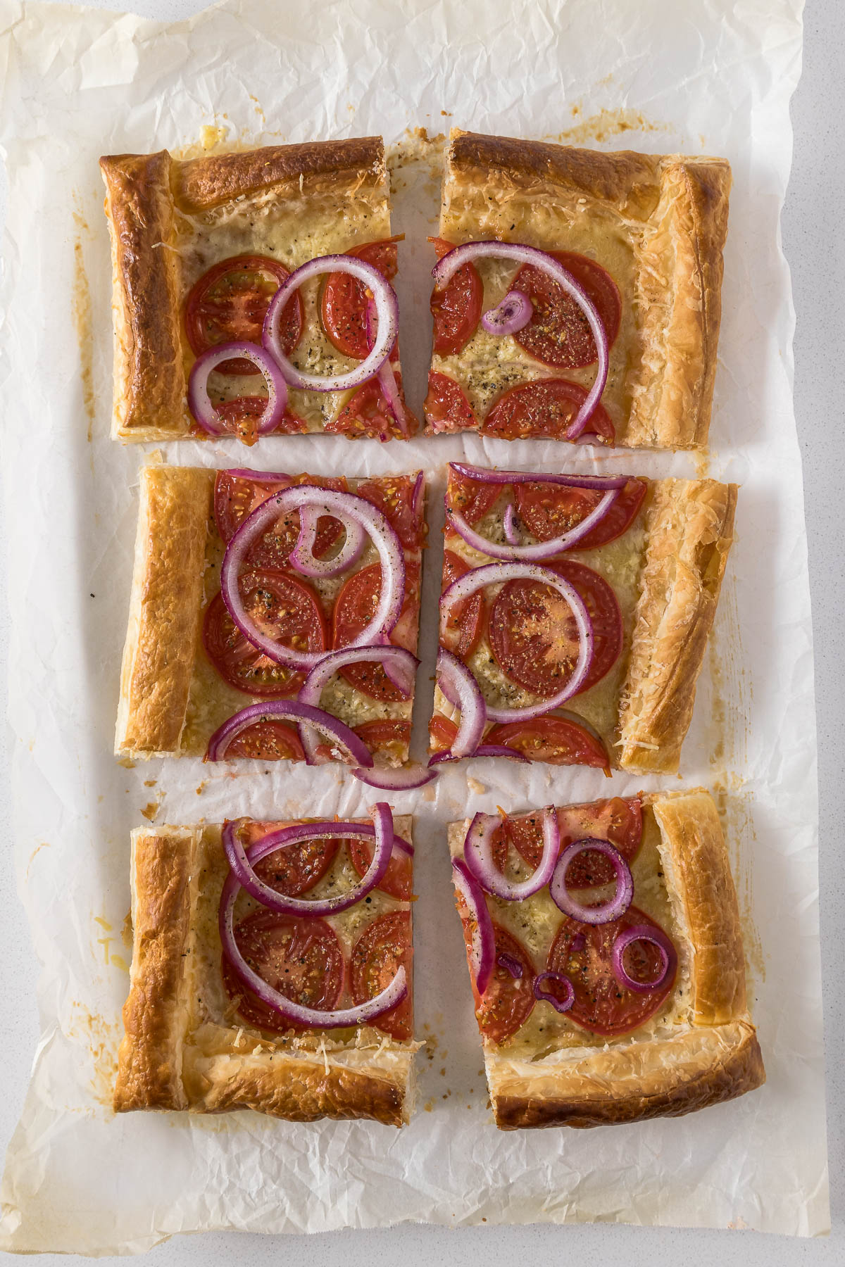 Sliced tomato puff pastry tart showing cheese, tomatoes and red onion.