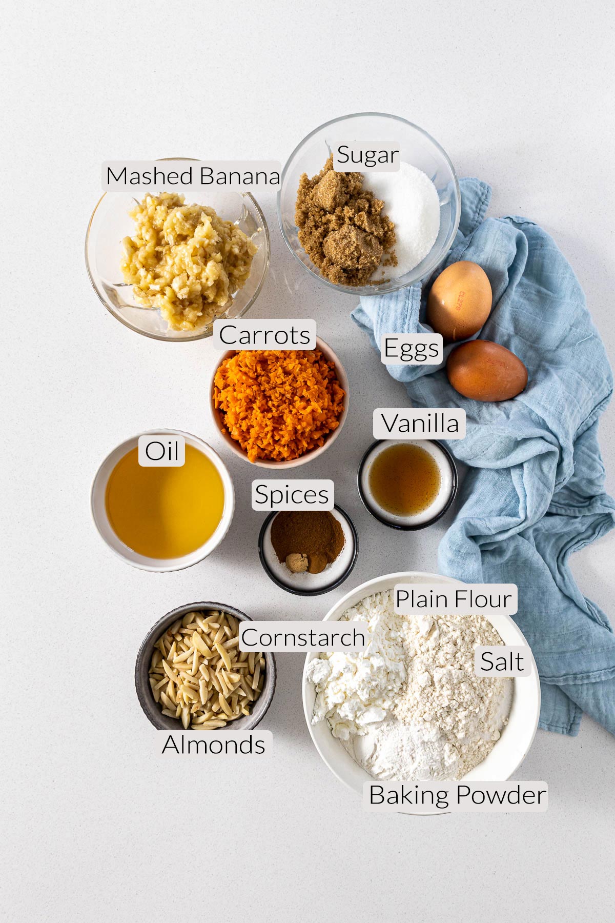 Banana and carrot muffins ingredients - flour, cornstarch, baking powder, salt, almonds, carrots, banana, spices, eggs, sugar, and vanilla.