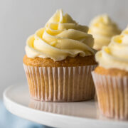 Vanilla cupcake with a large swirl of vanilla buttercream frosting on a cake stand.