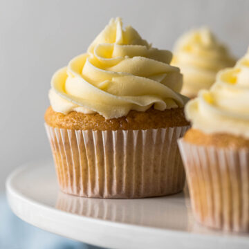 Vanilla cupcake with a large swirl of vanilla buttercream frosting on a cake stand.