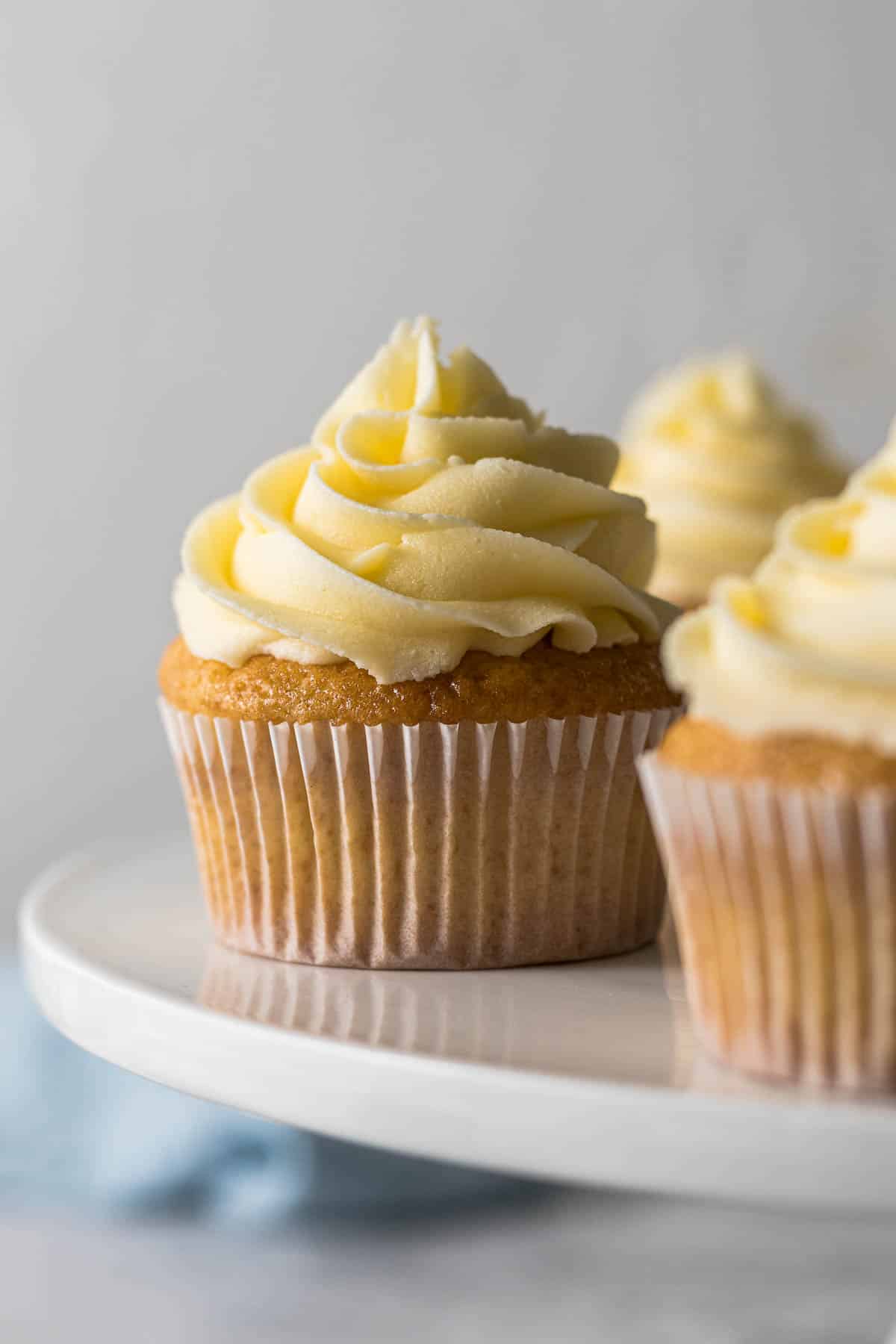 Vanilla cupcake with a large swirl of vanilla buttercream frosting on a cake stand.
