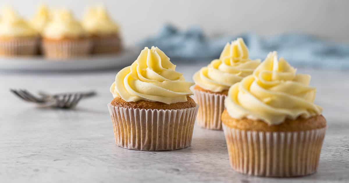Vanilla cupcake with a large swirl of vanilla buttercream frosting on a cake stand.