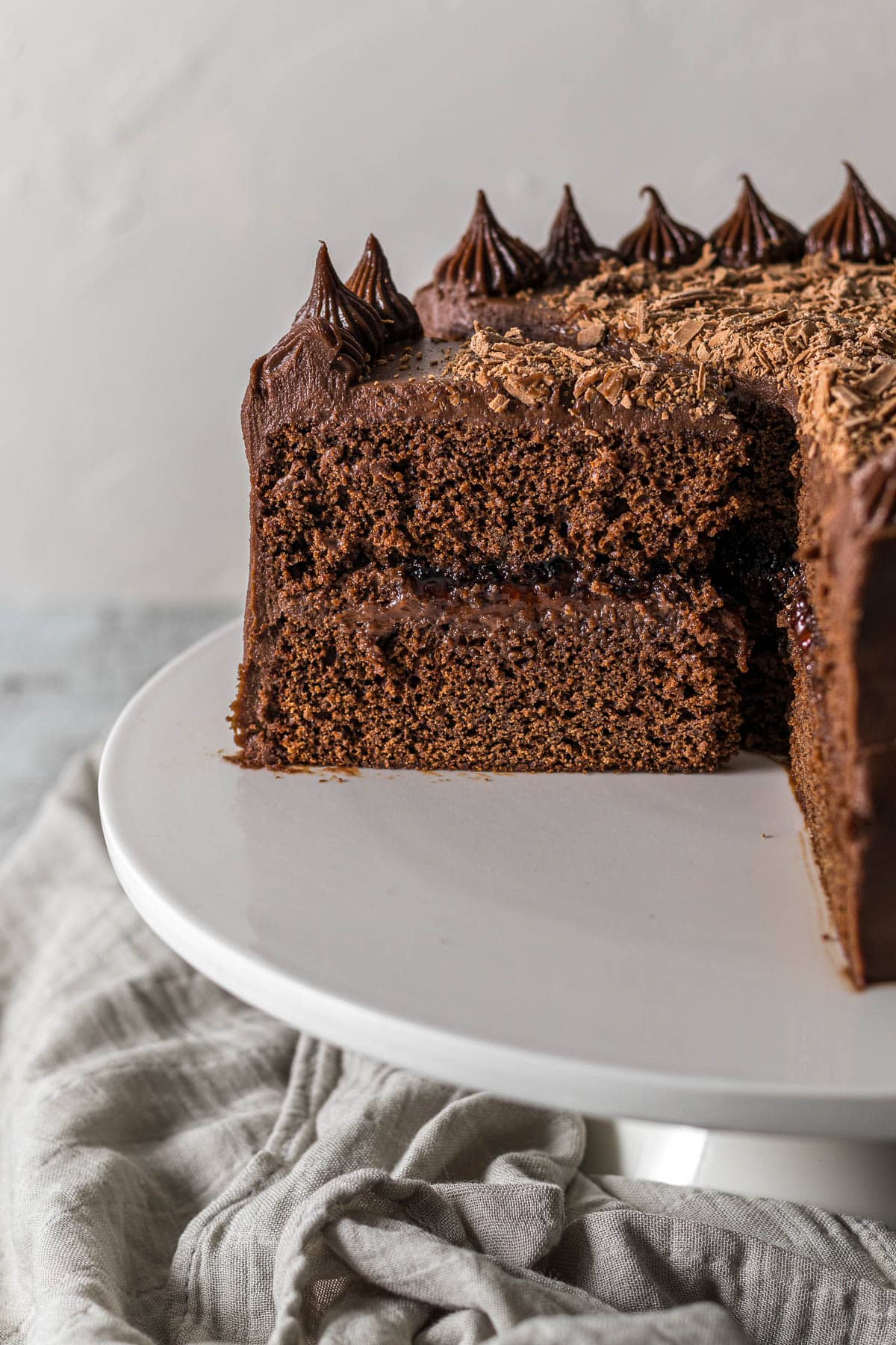 Sliced chocolate cake with cream cheese frosting on a cake stand.
