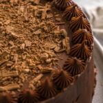 Chocolate cake with cream cheese frosting topped with flakey chocolate.