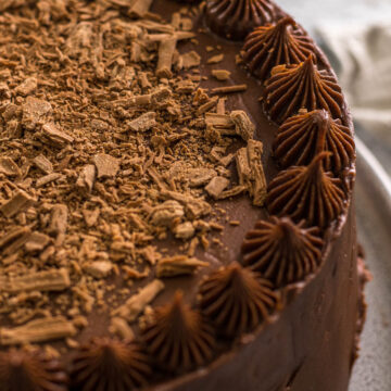 Chocolate cake with cream cheese frosting topped with flakey chocolate.