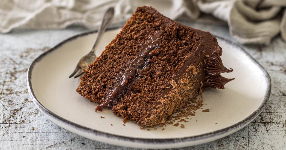 Slice of chocolate cake with cream cheese frosting topped with flakey chocolate.