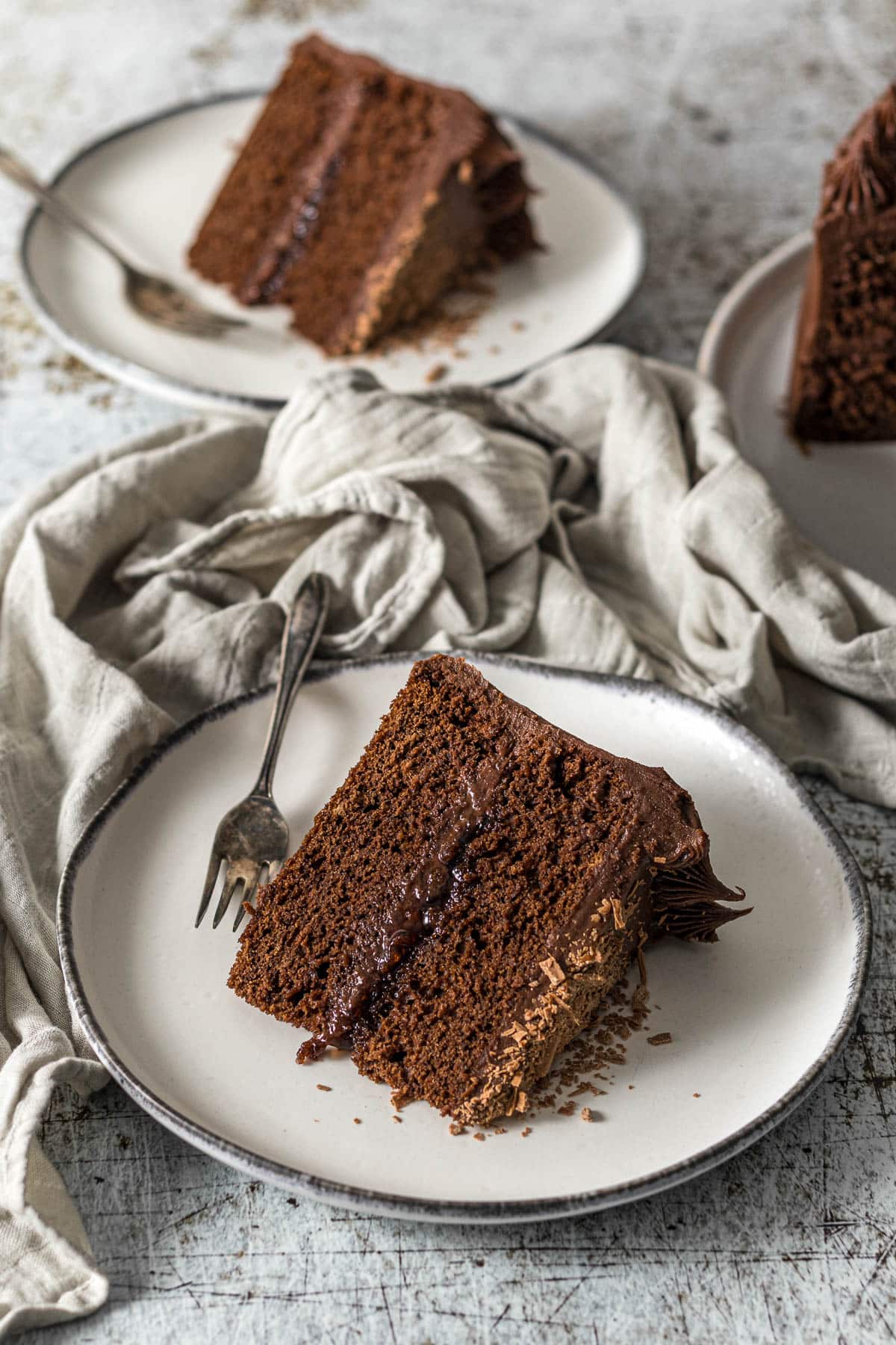 Slice of chocolate cake with cream cheese frosting topped with flakey chocolate.