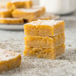 Three lemon bars stacked on each other with a dusting of icing sugar.