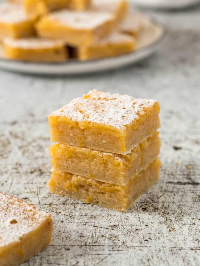 Three lemon bars stacked on each other with a dusting of icing sugar.