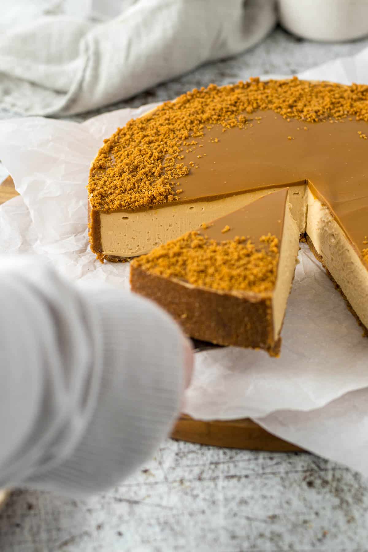 A hand picking up a slice of cheesecake with a cake server.