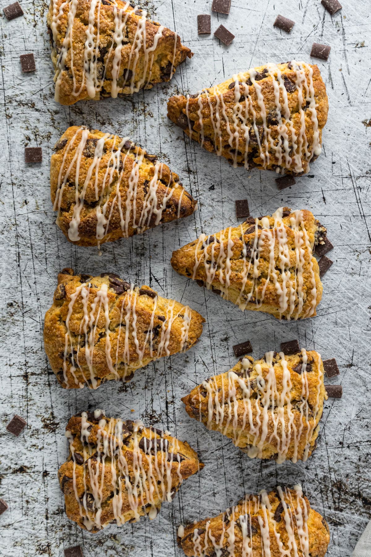 Chocolate chip scones with a sugar top and vanilla glaze on a counter.