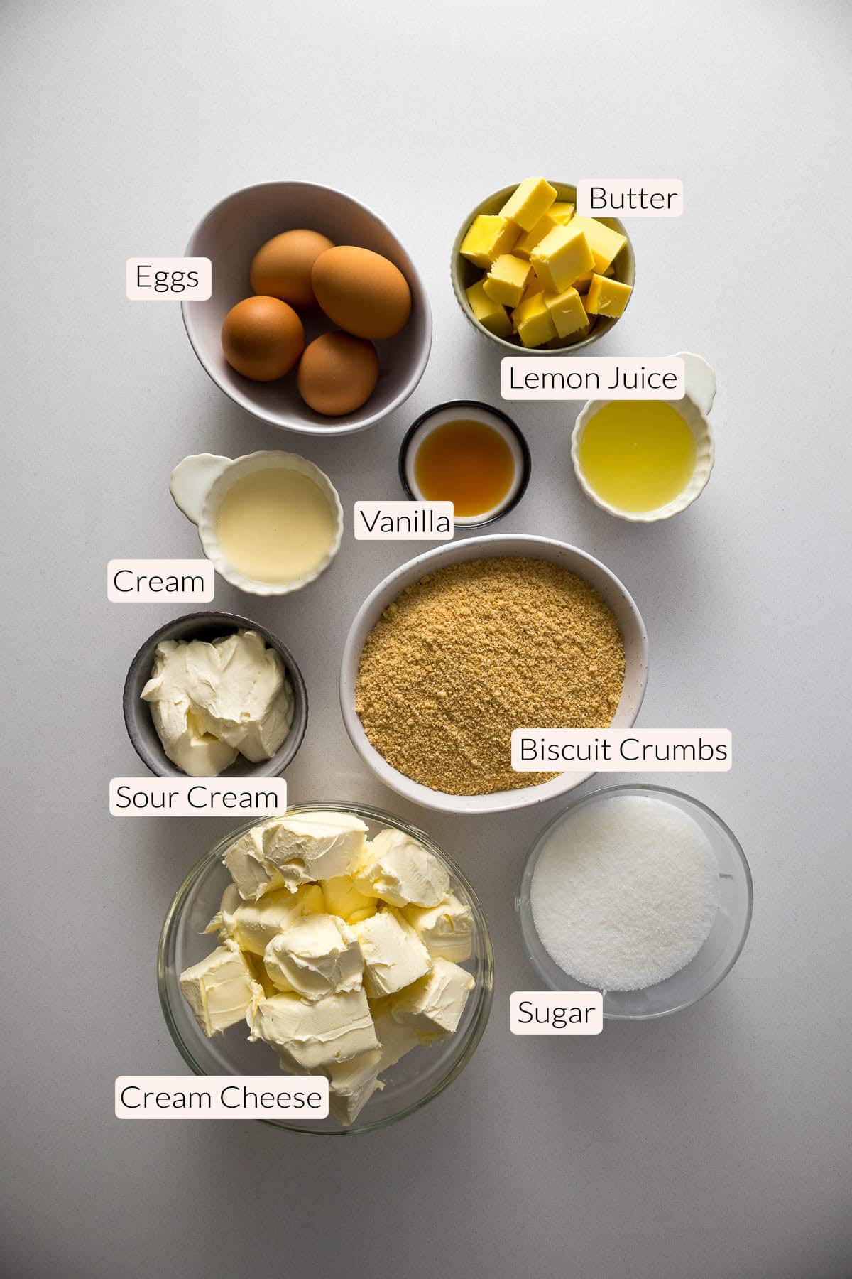 New York cheesecake ingredients - cream cheese, sour cream, cream, sugar, biscuit crumbs, butter, eggs, lemon juice, vanilla and eggs.