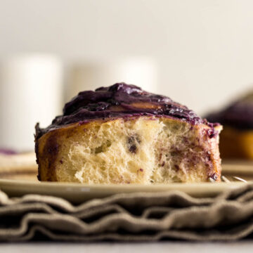 Cinnamon Blueberry roll on a plate with blueberry frosting.