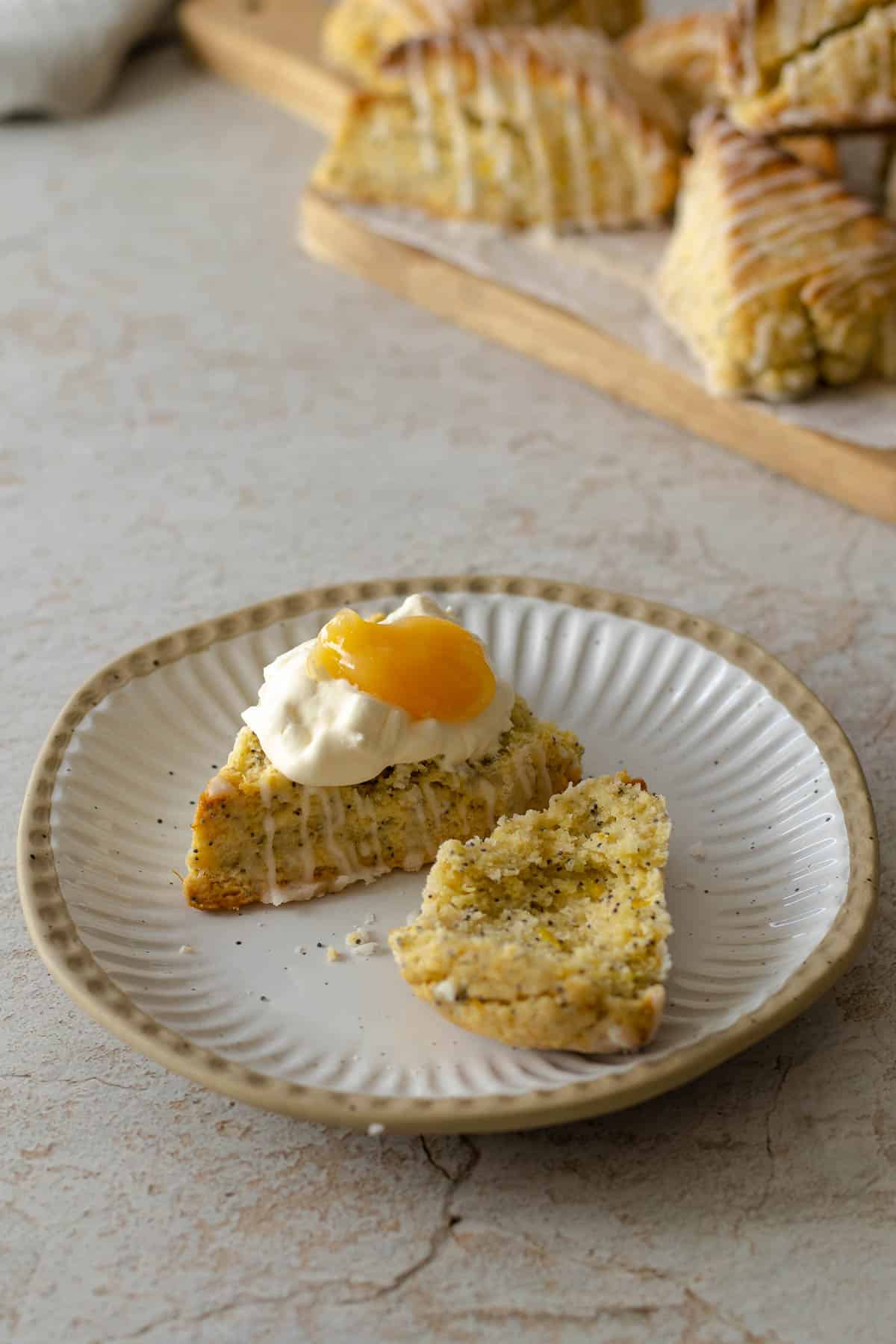 Lemon scone topped with whipped cream and lemon curd on a plate.