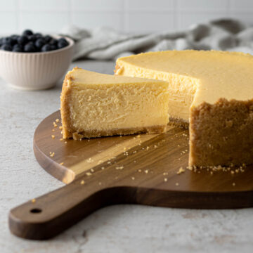 Slice of cheesecake next to the full cheesecake on a serving board.