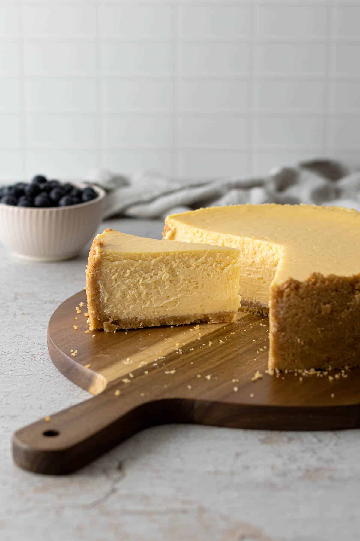 Slice of cheesecake next to a full cheesecake on a serving platter.