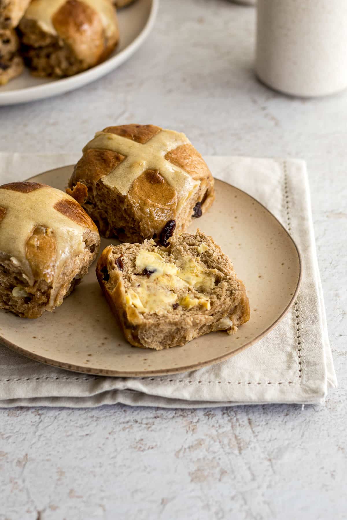 Hot cross buns on a plate, sliced with some butter.