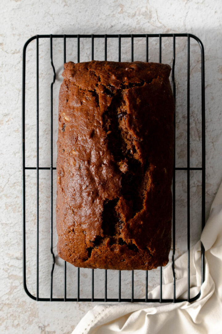 Date and walnut loaf cooling on a wired rack, showing the beautiful crack down the center.