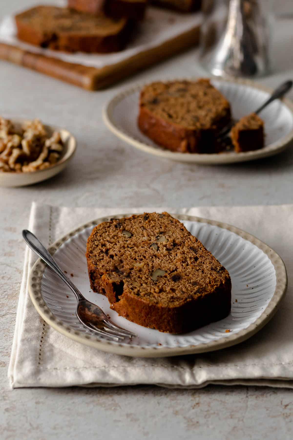 A slice of walnut date cake on a plate with a cake fork.