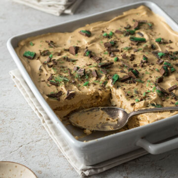 Peppermint crisp tart in a serving dish, with a serving spoon, sprinkled with pieces of peppermint crisp.