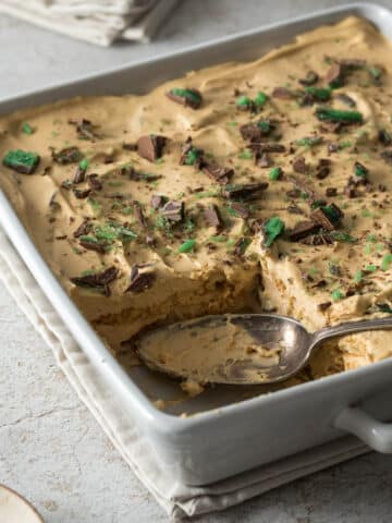 Peppermint crisp tart in a serving dish, with a serving spoon, sprinkled with pieces of peppermint crisp.